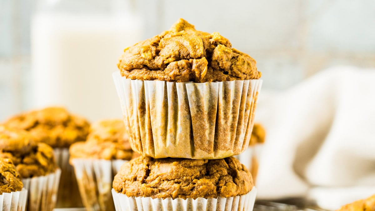 Two gluten free pumpkin muffins stacked with muffins in background.