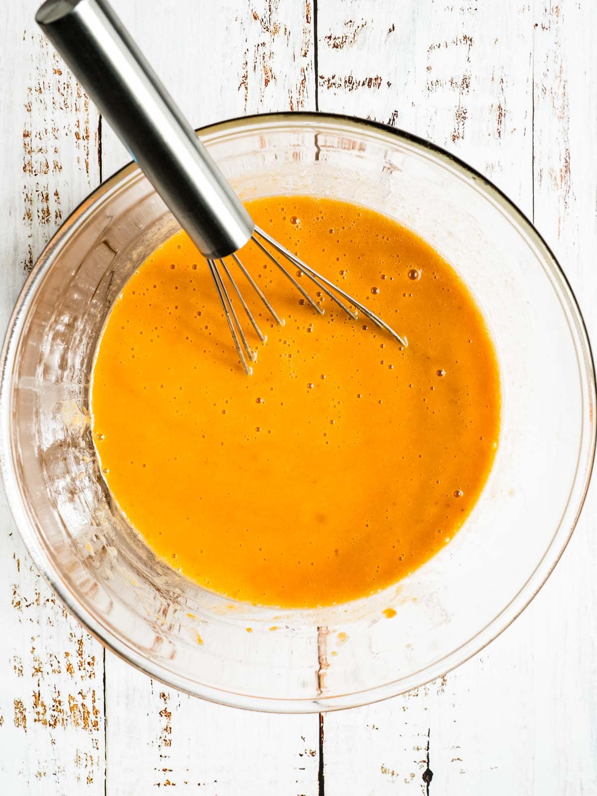 Wet ingredients whisked in clear bowl for gluten free pumpkin muffins.