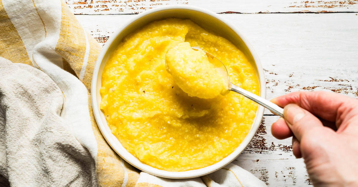 Creamy baked polenta in white bowl with a scoop held up by a spoon.