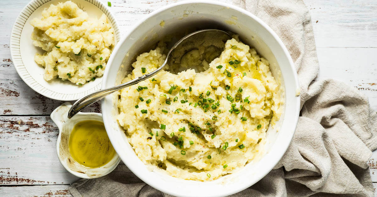 Garlic mashed potatoes in a white serving dish with spoon and extra olive oil on the side.