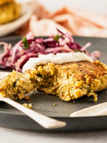 Chickpea burger with vegan mayo, slice of lemon, and coleslaw on black plate.